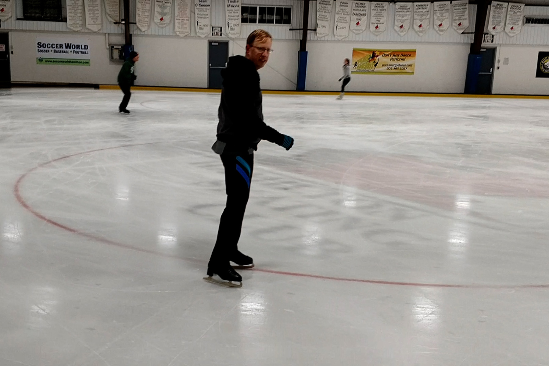 A middle aged blond man on figure skates, on a hockey rink.