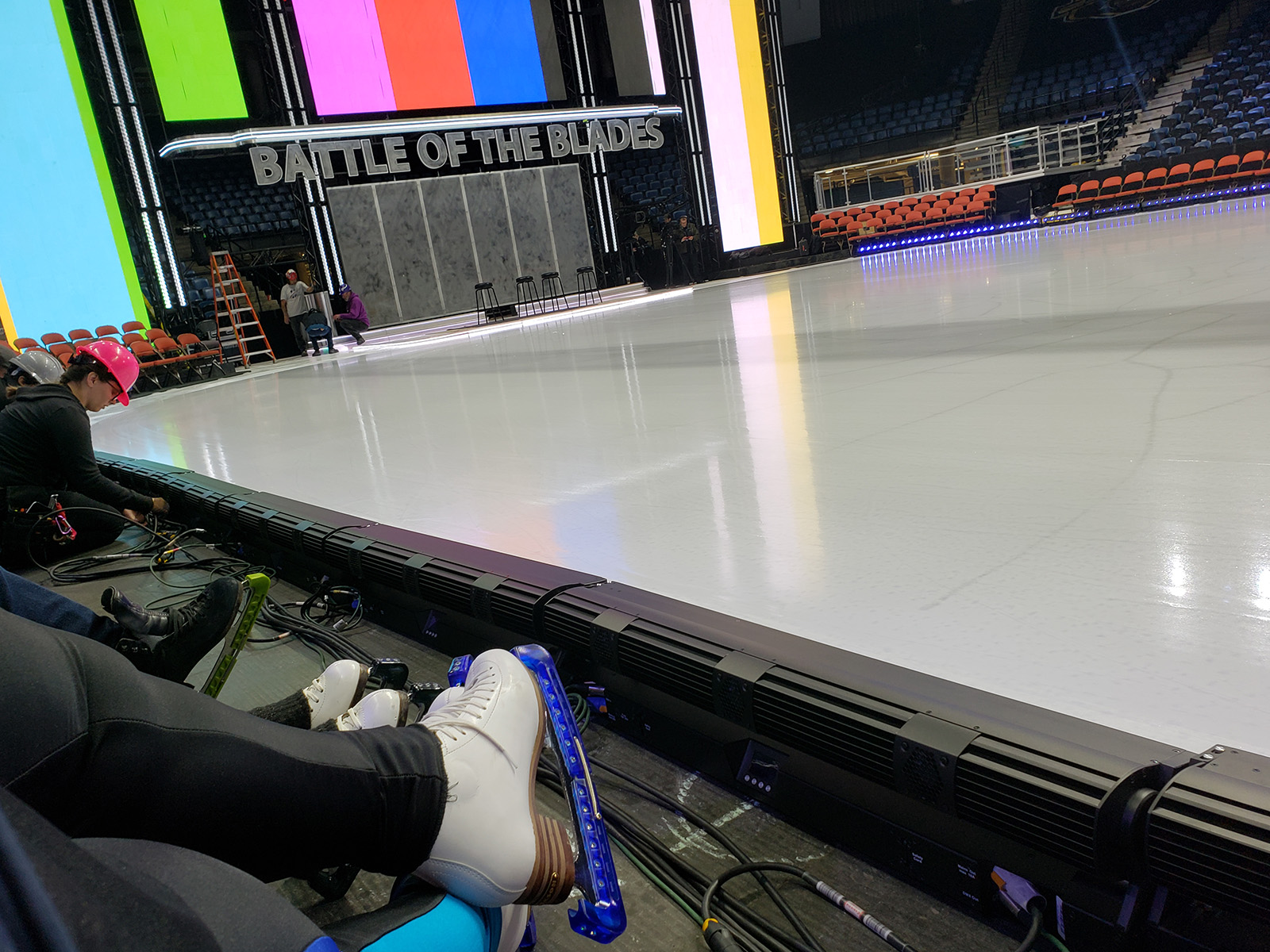 A pair of crossed figure skater legs in front of an ice rink.