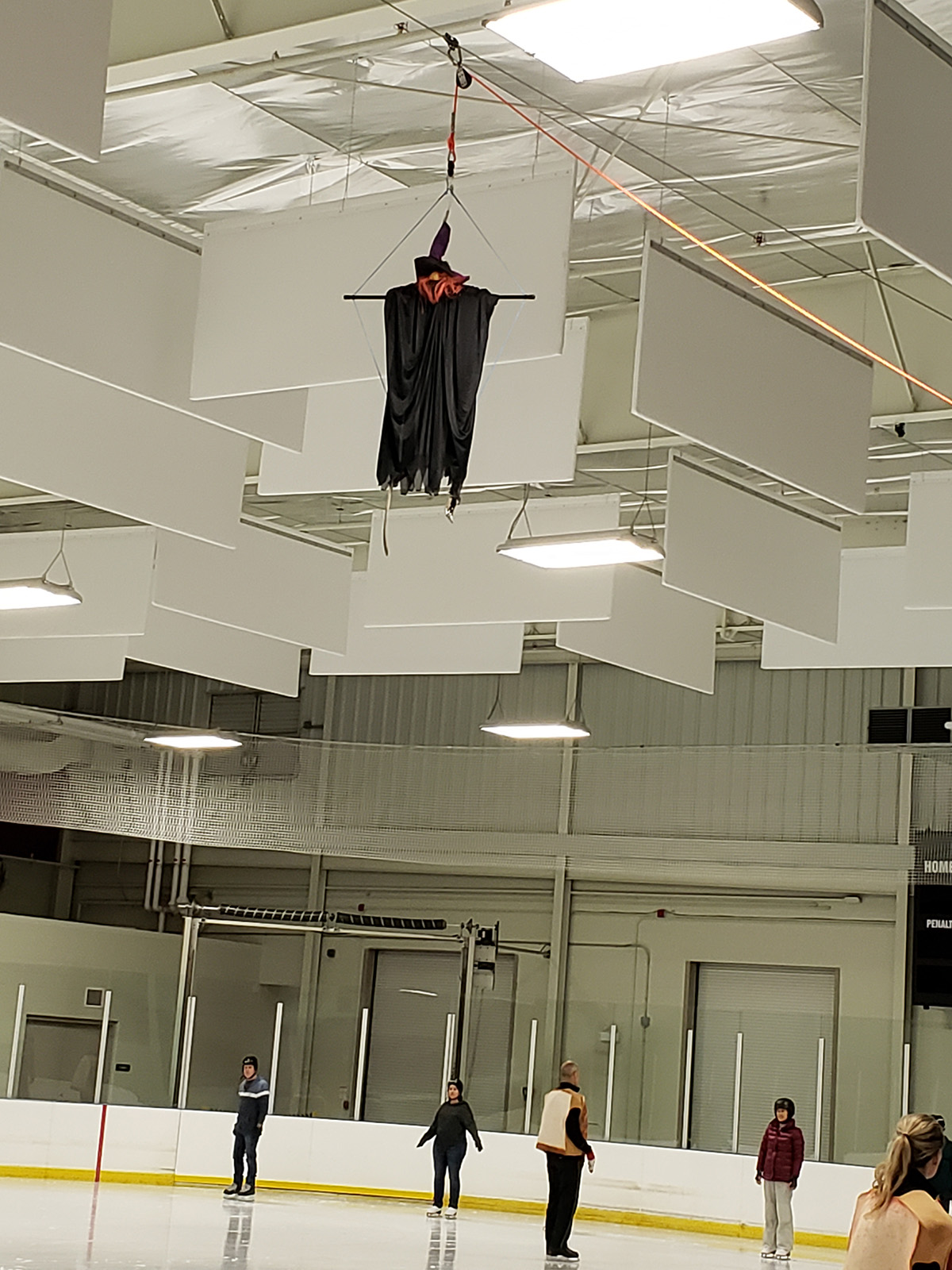 A witch decoration hanging from the rafters of an ice rink.