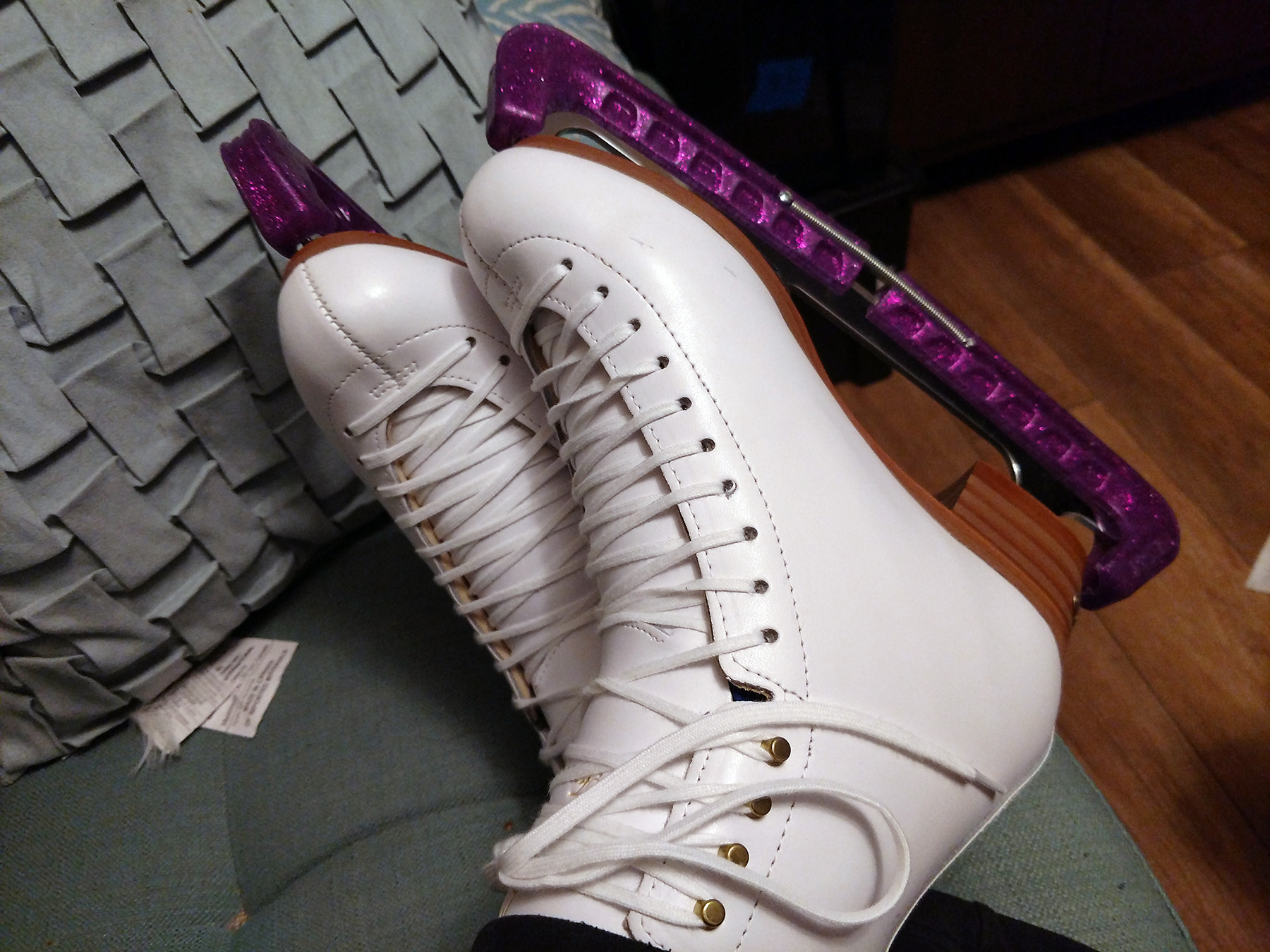 White figure skates on feet, with purple glittery blade guards.