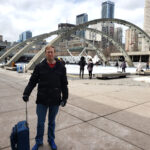 A middle ages man with a skate bag, standing in front of Nathan Phillips Square.