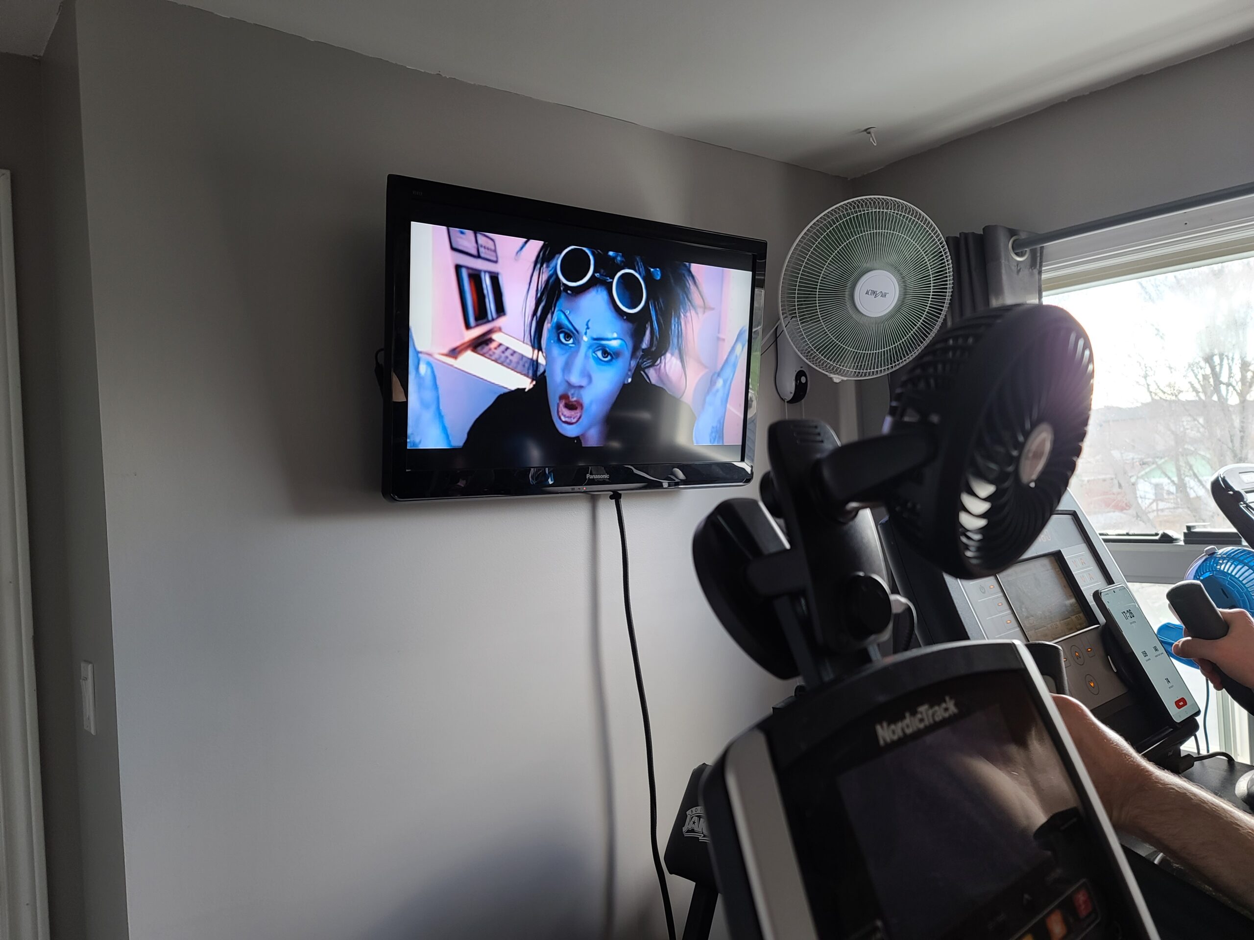 Simone Denny on a home gym TV, behind some cardio equipment.