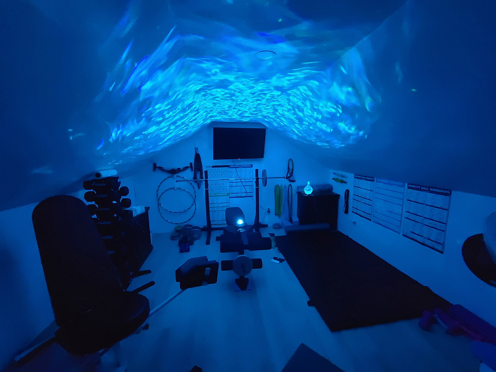 A home gym illuminated in blue, with a galaxy light projection on the ceiling.