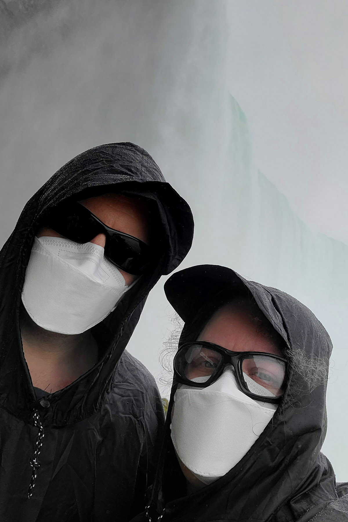 A masked couple poses on front of Niagara Falls.